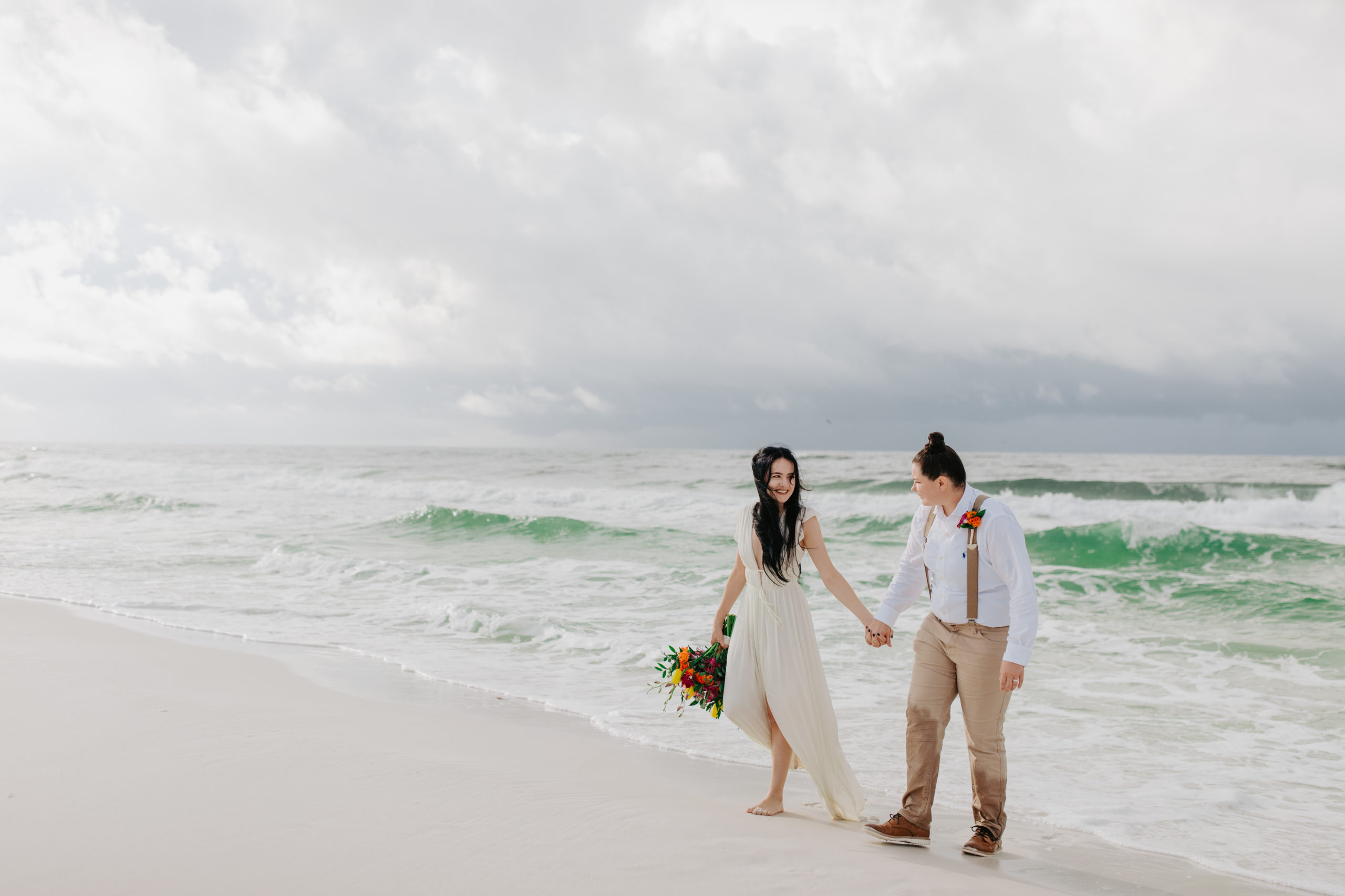 How to Elope In Texas Celebration Article - same sex couple walking on the beach on their wedding day near the Ocean. 