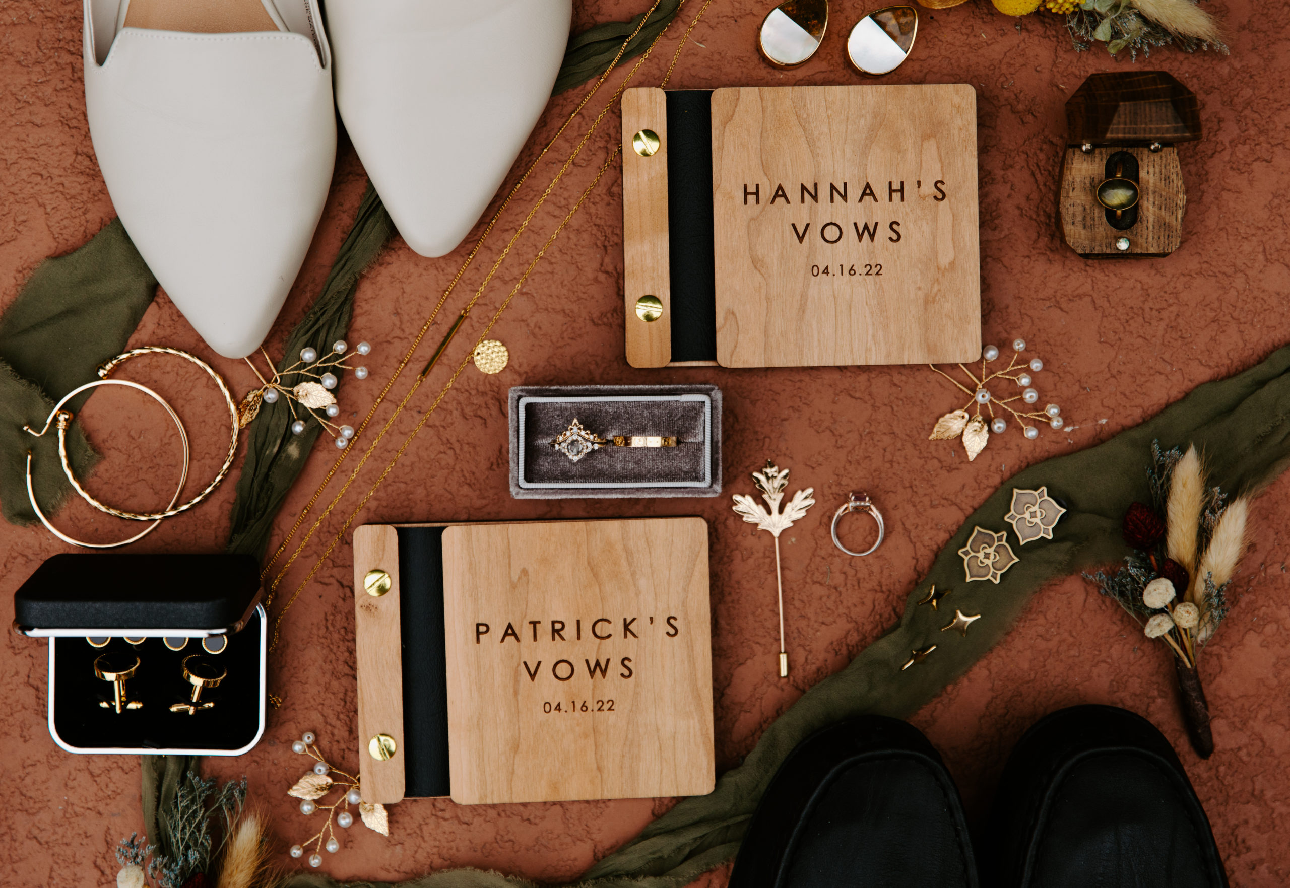 a flatlay detail shot of wedding day items such as a custom vowbook, wedding rings, pins, gold necklaces. 