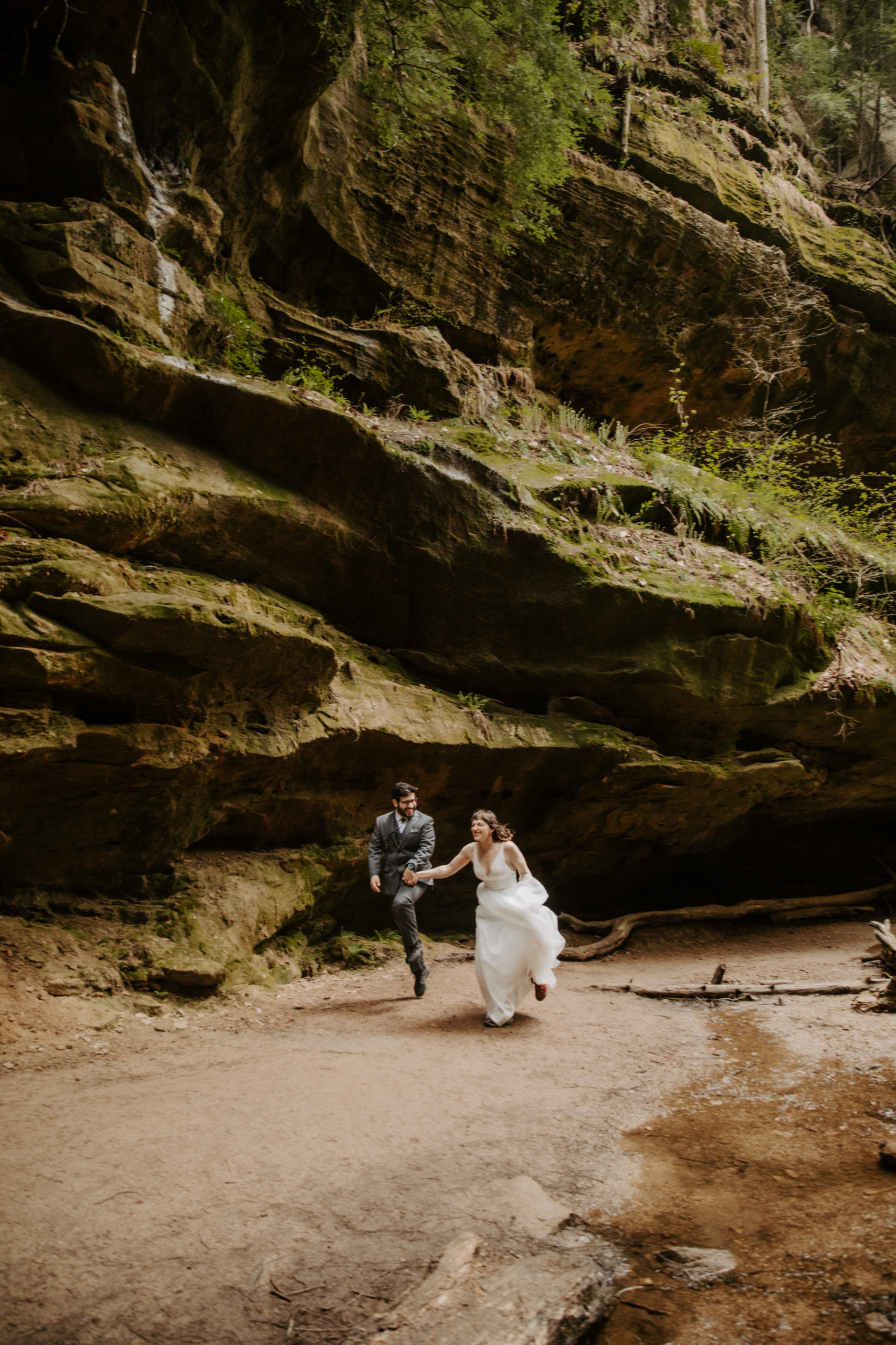Bride and Groom running to their elopement spot in Conkle Hollow next to mossy rocks and a stream.