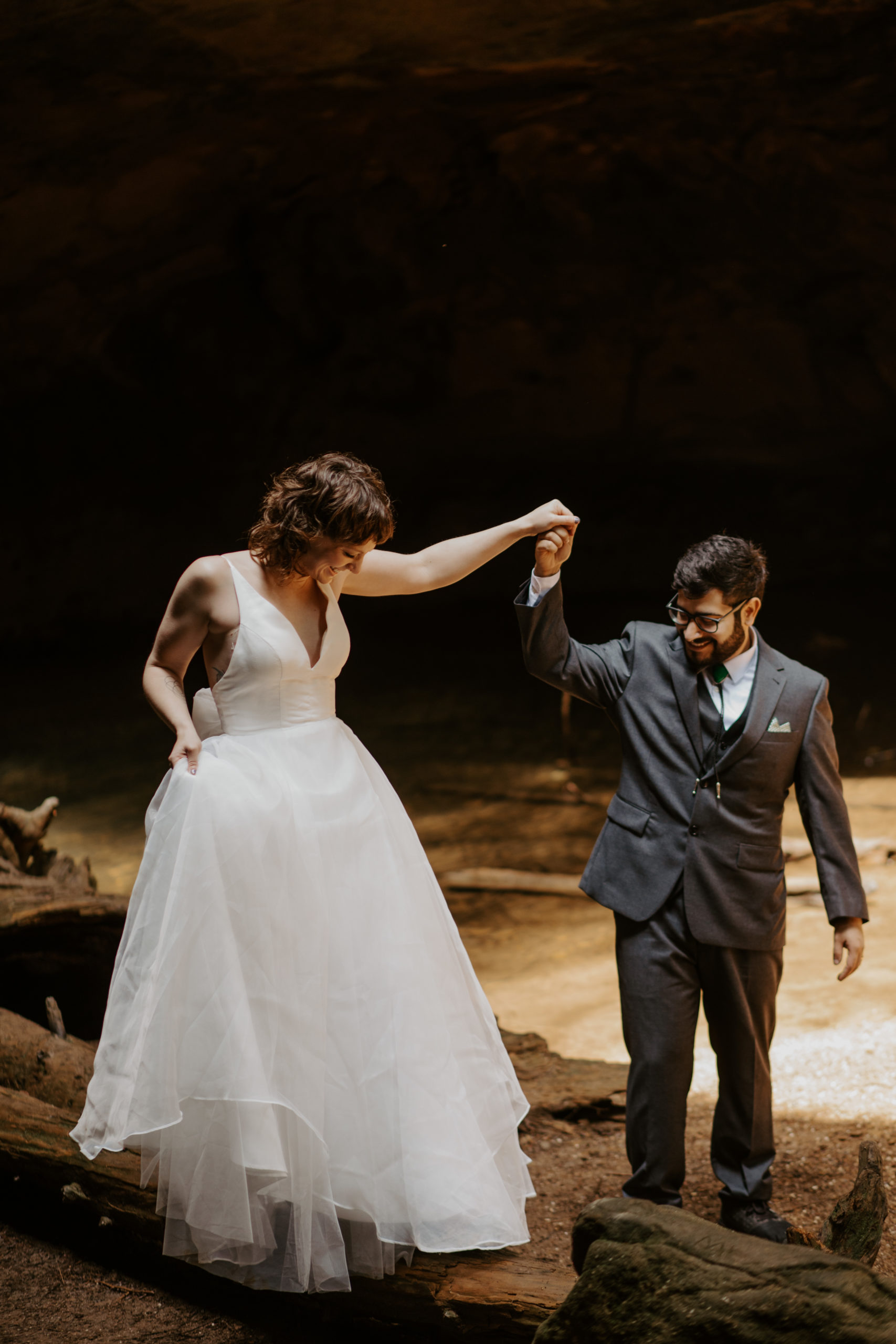 A wedding couple leading each other across a stream while adventuring around the Conkle's hollow Trail on their elopement day at Hocking Hills