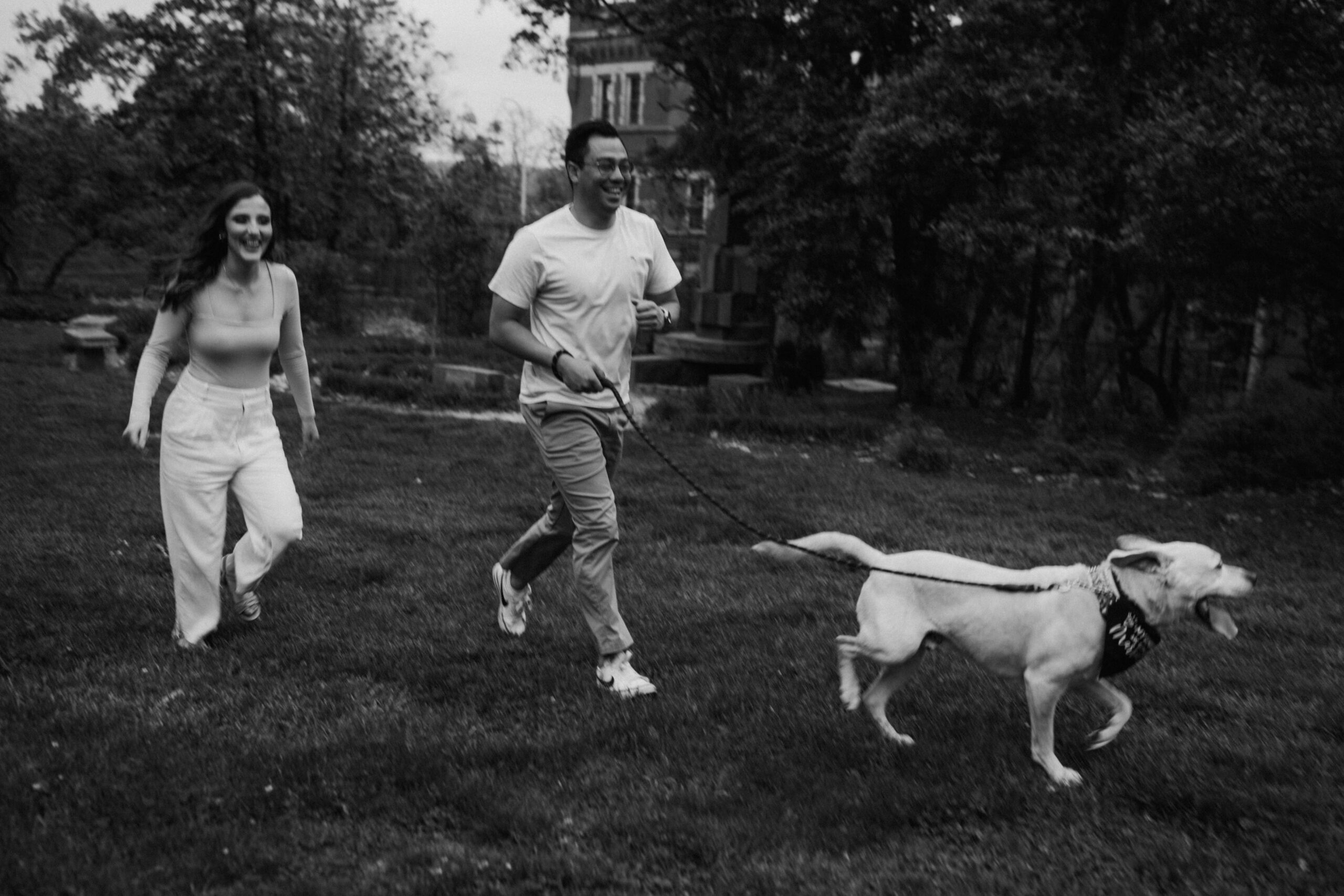 A couple running with their dog outside at a park during their engagement session.