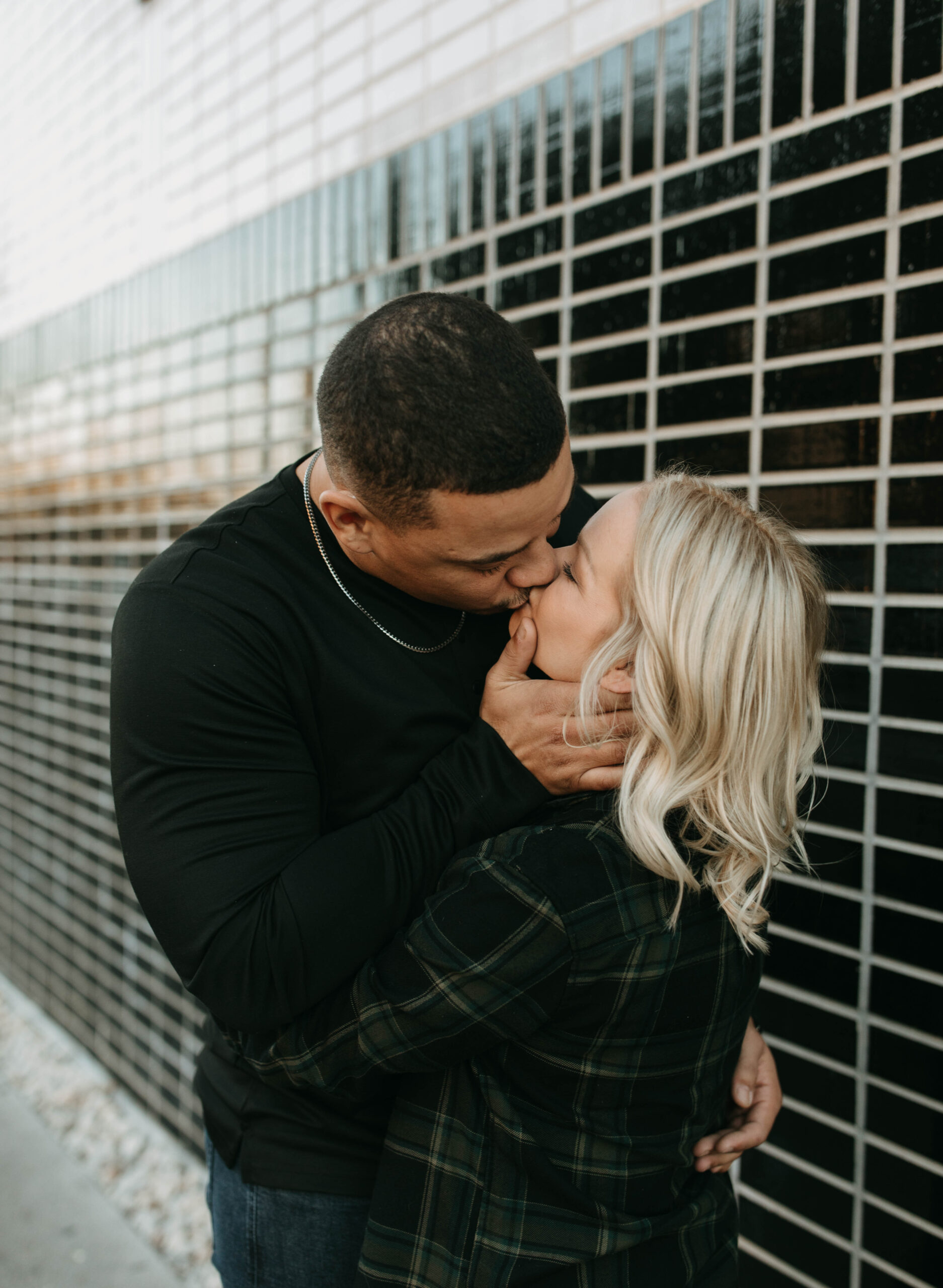 Candid engagement photography on south congress avenue in Austin Texas. A photo of an engaged couple is kissing in front of black stone wall. 