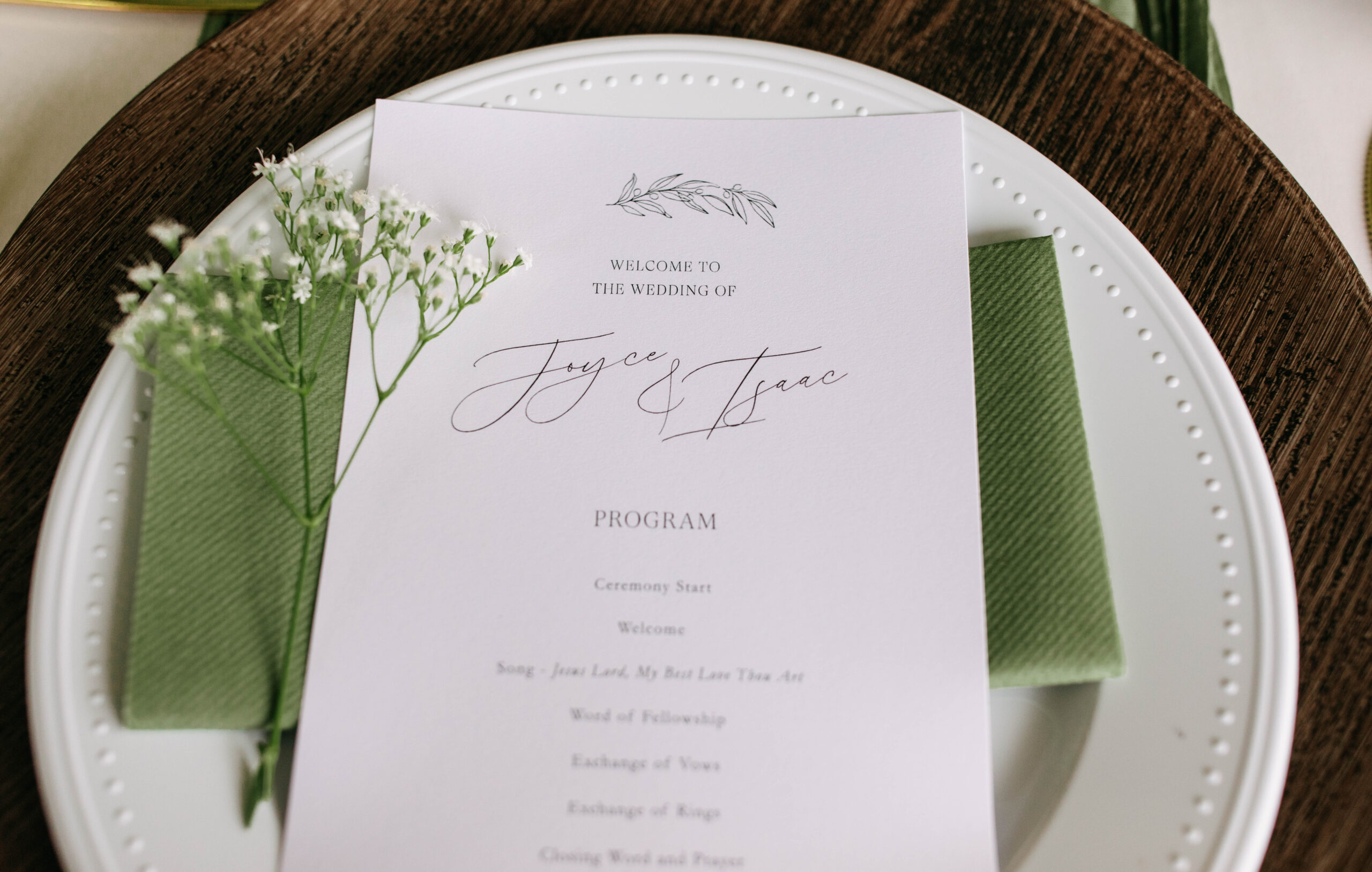 An up close photograph of a wedding program on a place setting at a wedding reception. The wedding was an Austin wedding at Bear Creek Retreat. The reception place setting has green napkins and baby breath.