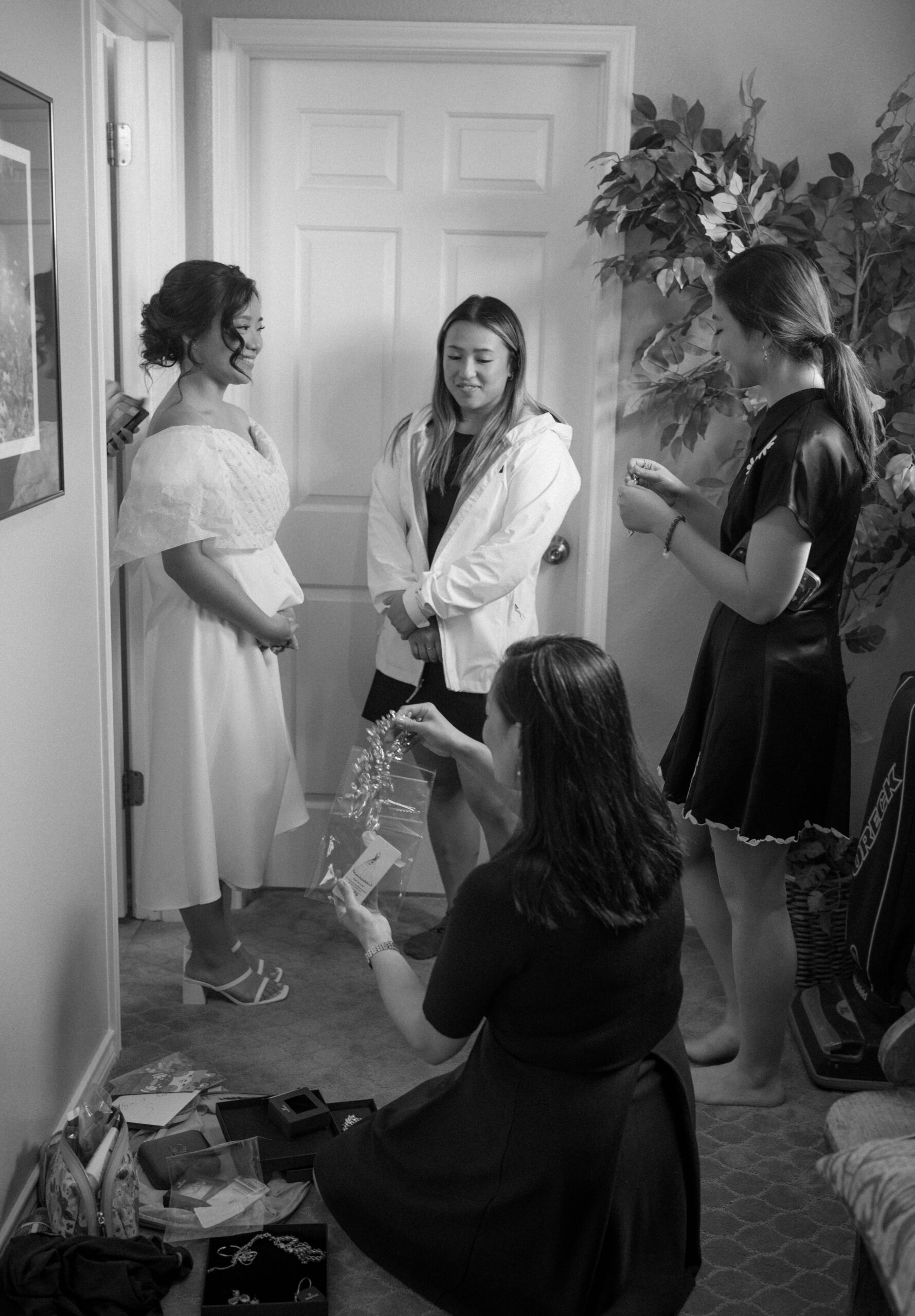 A black and white photograph of a bride getting ready on her Austin wedding day. She is surrounded by her friends helping her get dressed and do her makeup.