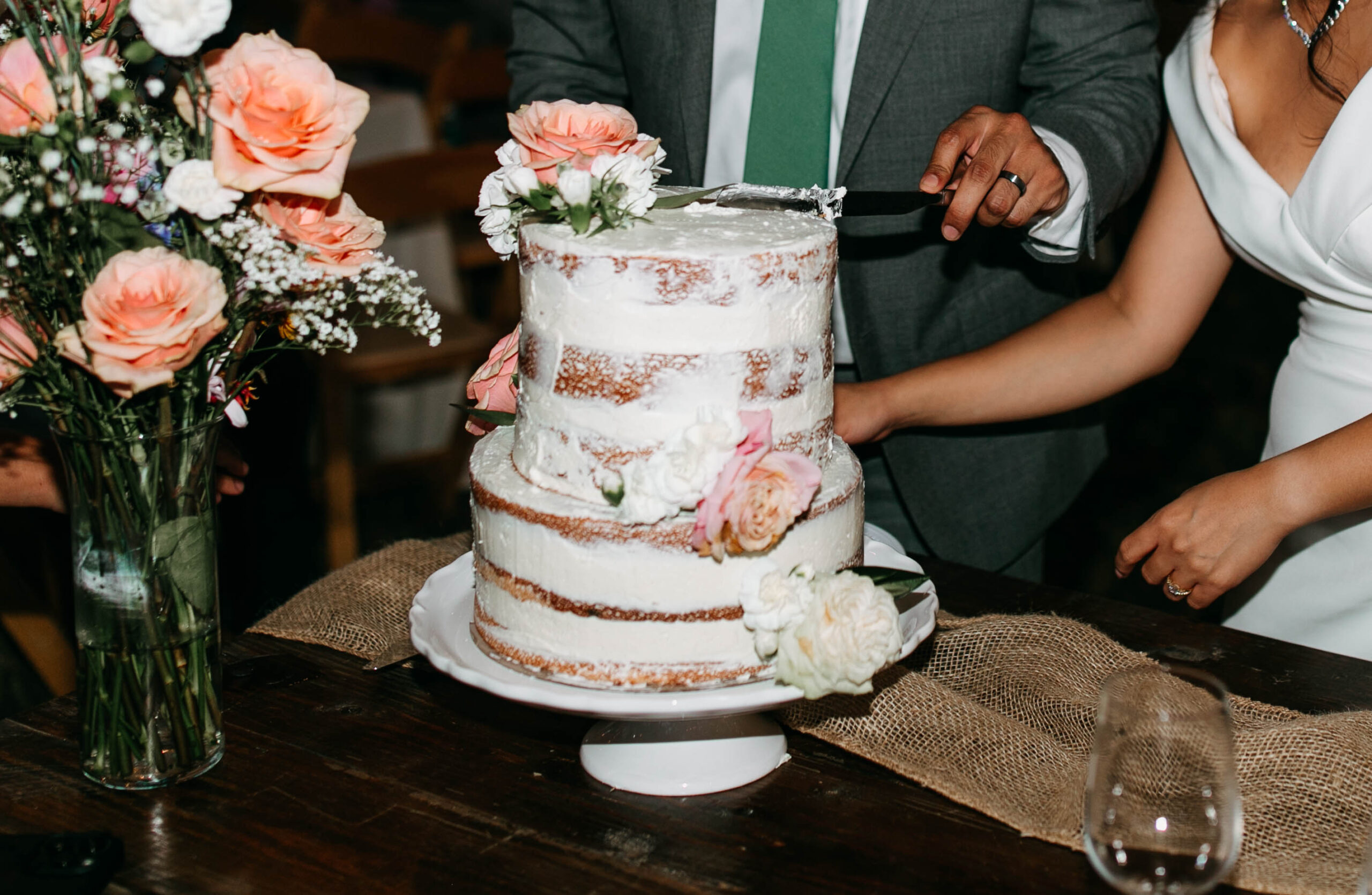 A naked wedding cake with pink and white rose decorations. 