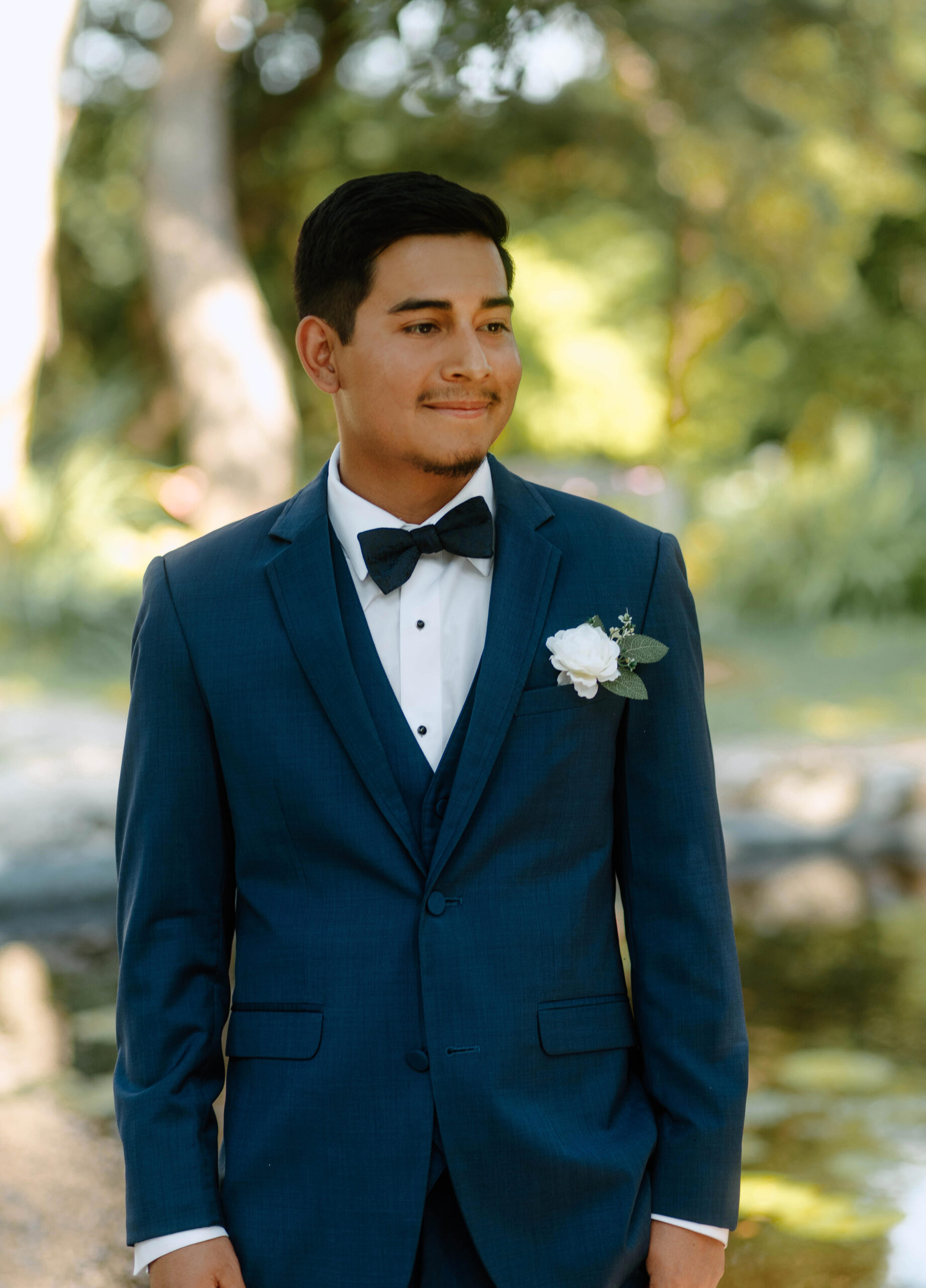 A wedding photograph of a groom wearing a blue suit with a black bowtie. 