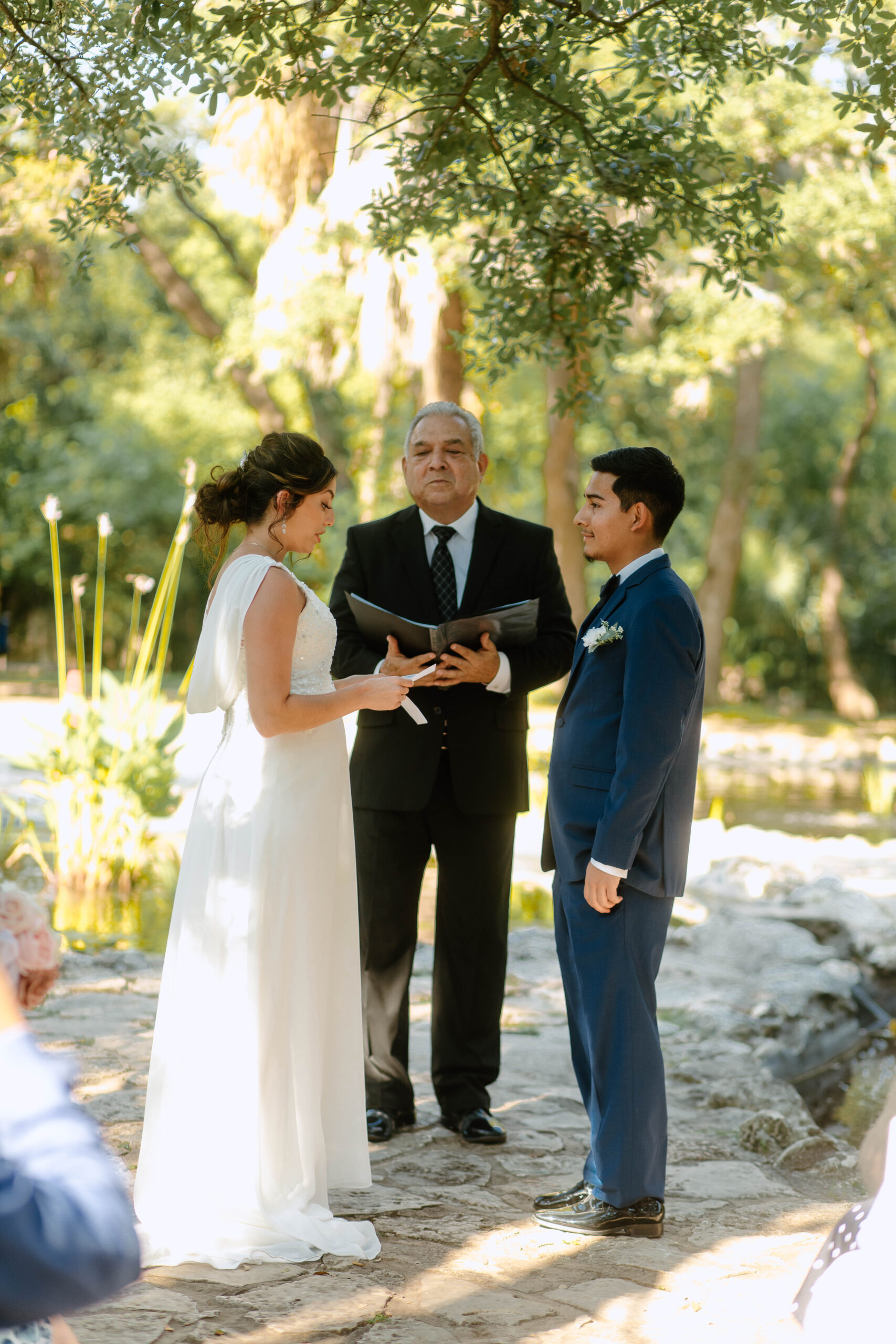 Couple exchanging vows at their Mayfield Garden Wedding in the summer. Mayfield Gardens is located in Austin, Texas.