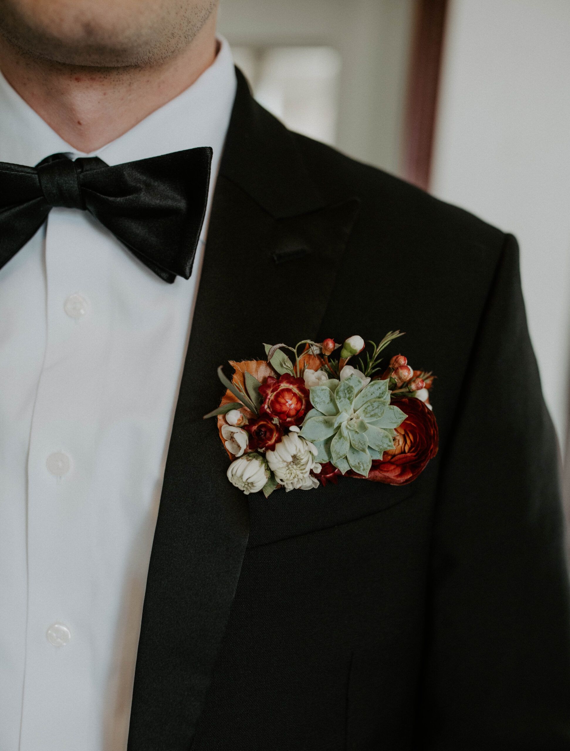 Detail photo of grooms floral pocket with succulents and red florals.