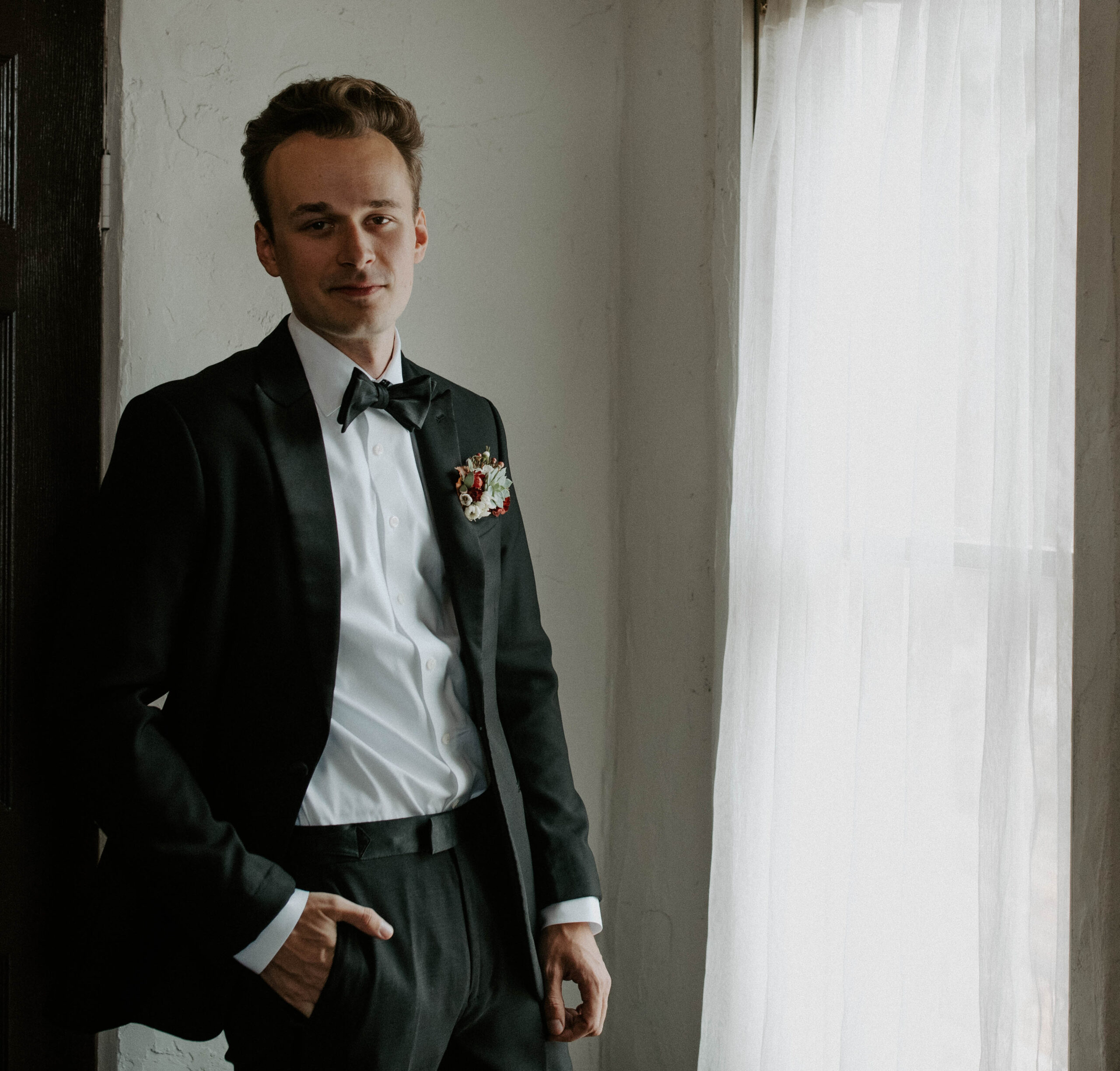 Black and white wedding photo of groom getting ready on his wedding day. The groom is wearing a classic black suit, white shirt and black bowtie.