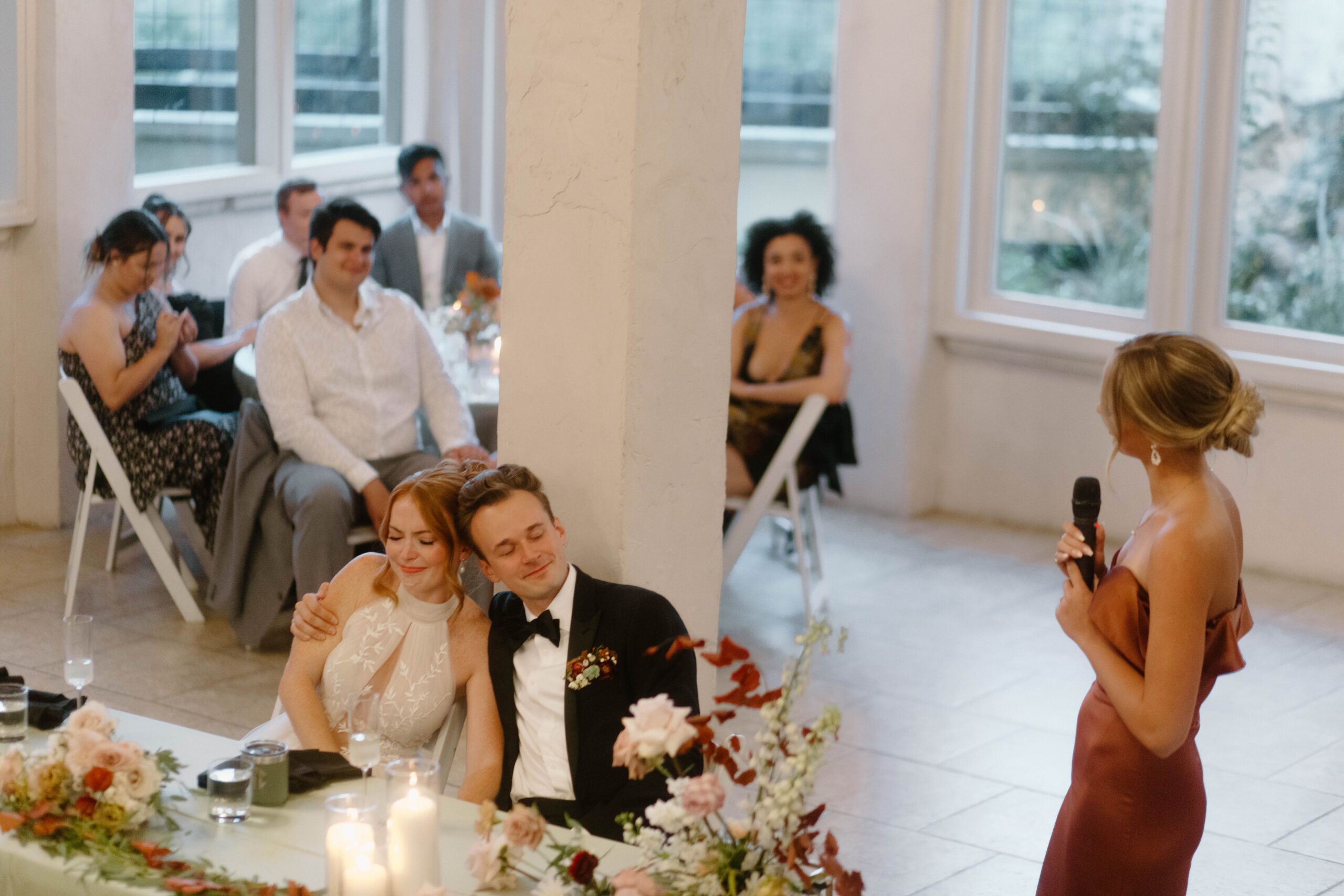 Newlyweds laughing during toasts at their wedding. The wedding took place at Villa Antonia in Austin Texas. They are enjoying a candlelit dinner with fresh florals and green linens. 
