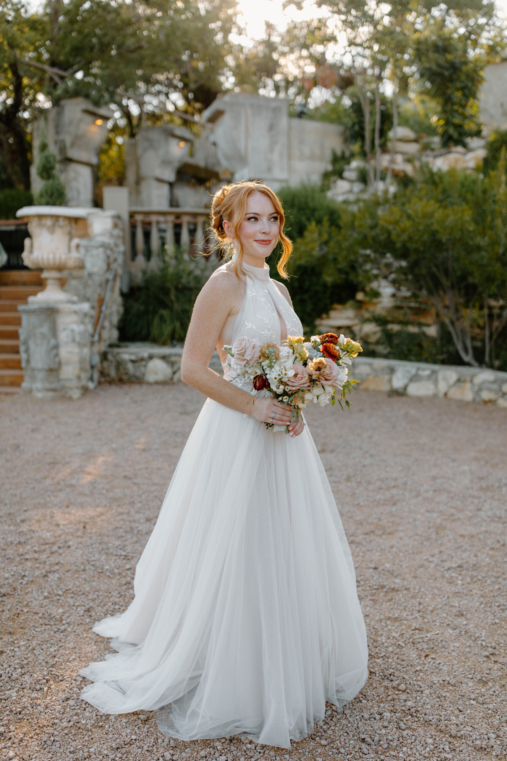 Bridal Portraits taken at Villa Antonia. A red haired bride in a halter neck wedding gown, featuring an autumn bouquet of roses. Courtyard wedding photos. 